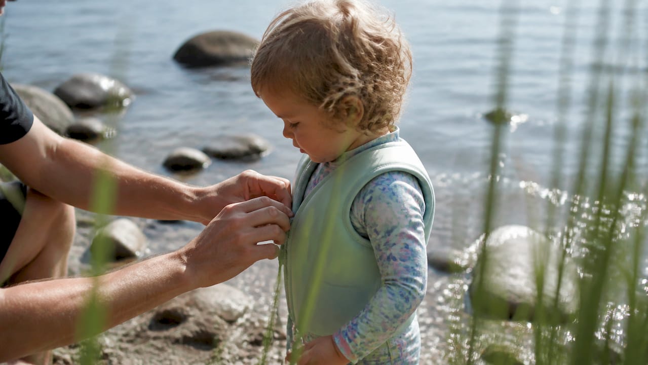 Ein Kleinkind zieht sich die Schwimmweste über das UV-Shirt an.