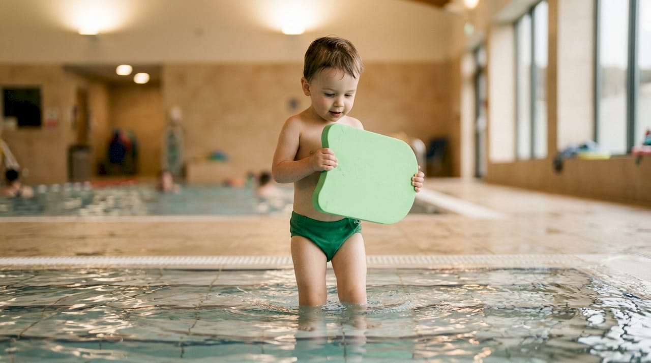 Kind übt Schwimmen mit Schwimmbrett im Hallenbad